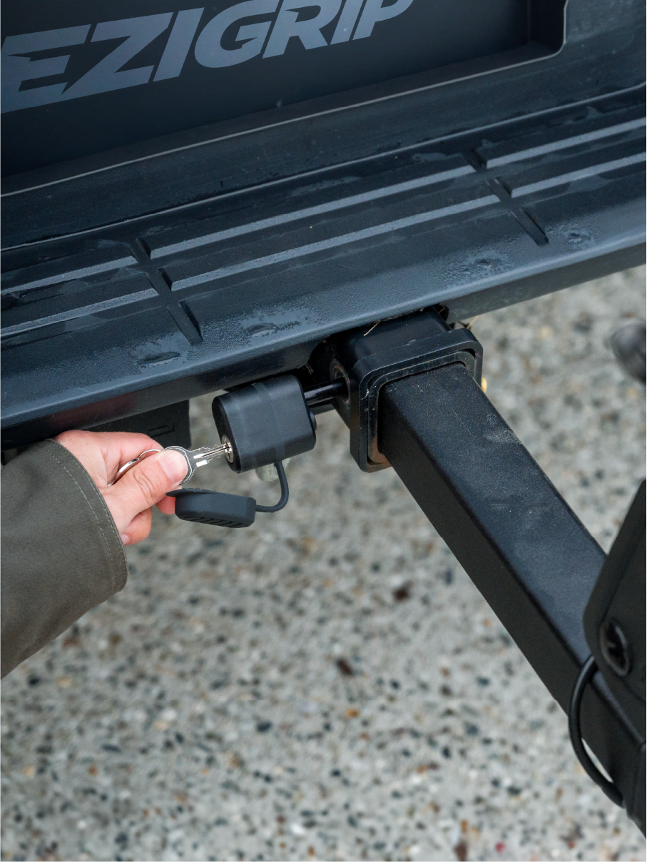 A close view of a hand locking the hitch pin that secures the E-Rack 2 Pro bike rack to the vehicle.
