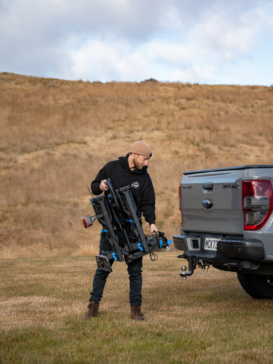 A man is approaching a truck with the E-Rack 2 Pro neatly folded and being easily carried to the ute