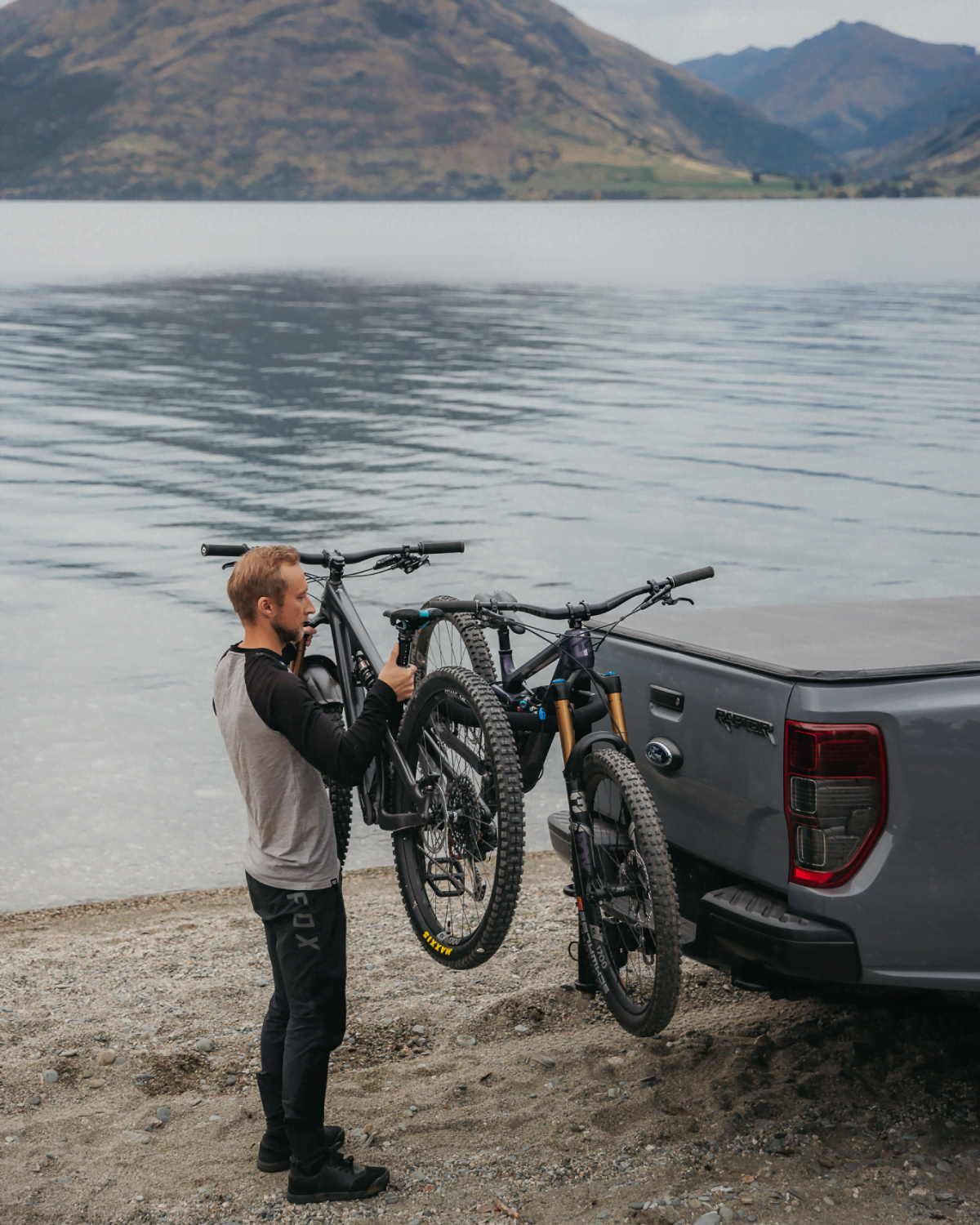 a man lifts a mountain bike onto an ezigrip advantage 2 bike rack that is moutned to a ute, beside a beautiful lake