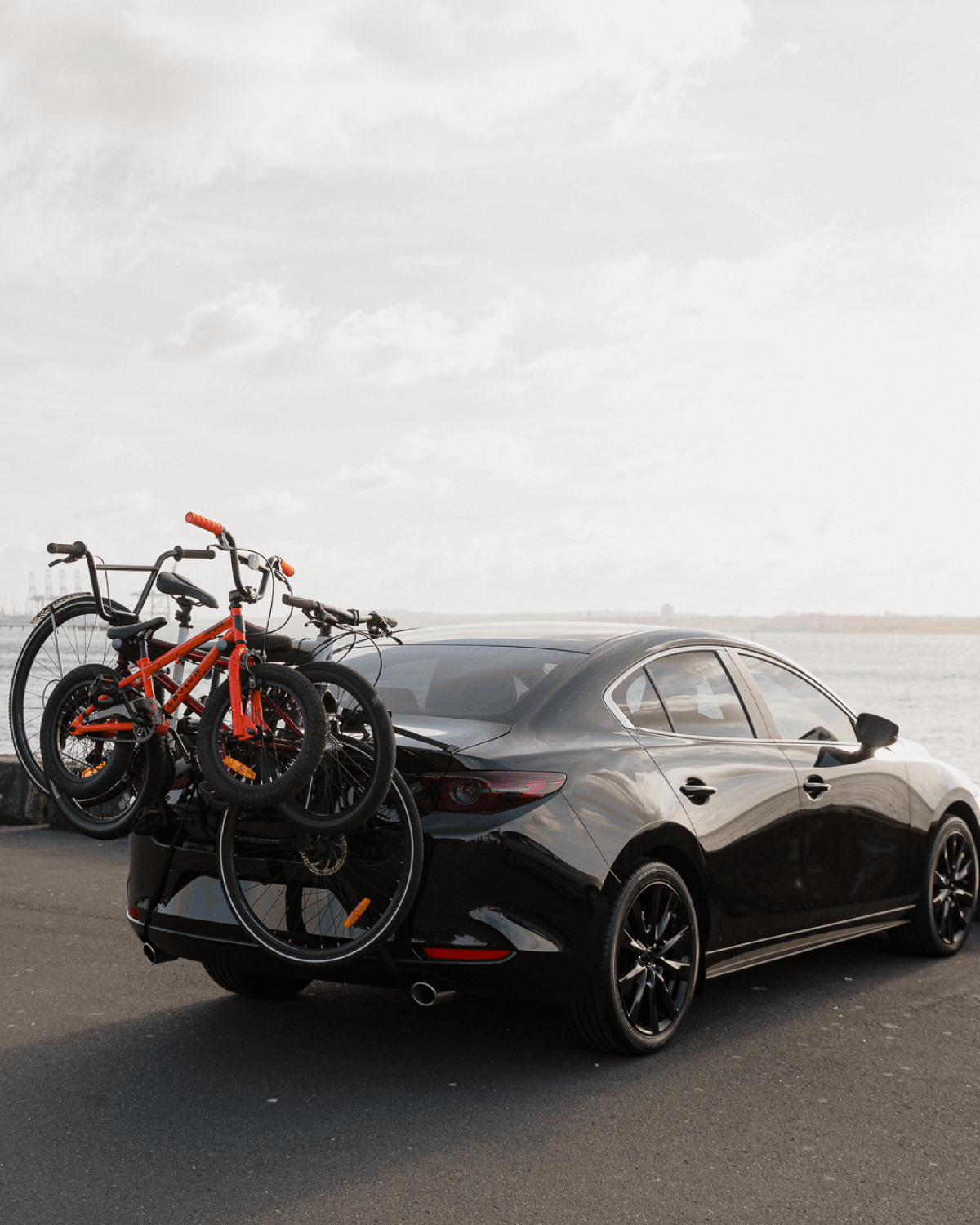 A Bootmount 3 pro bike rack is strapped to a sedan with 3 bikes loaded on the bike rack