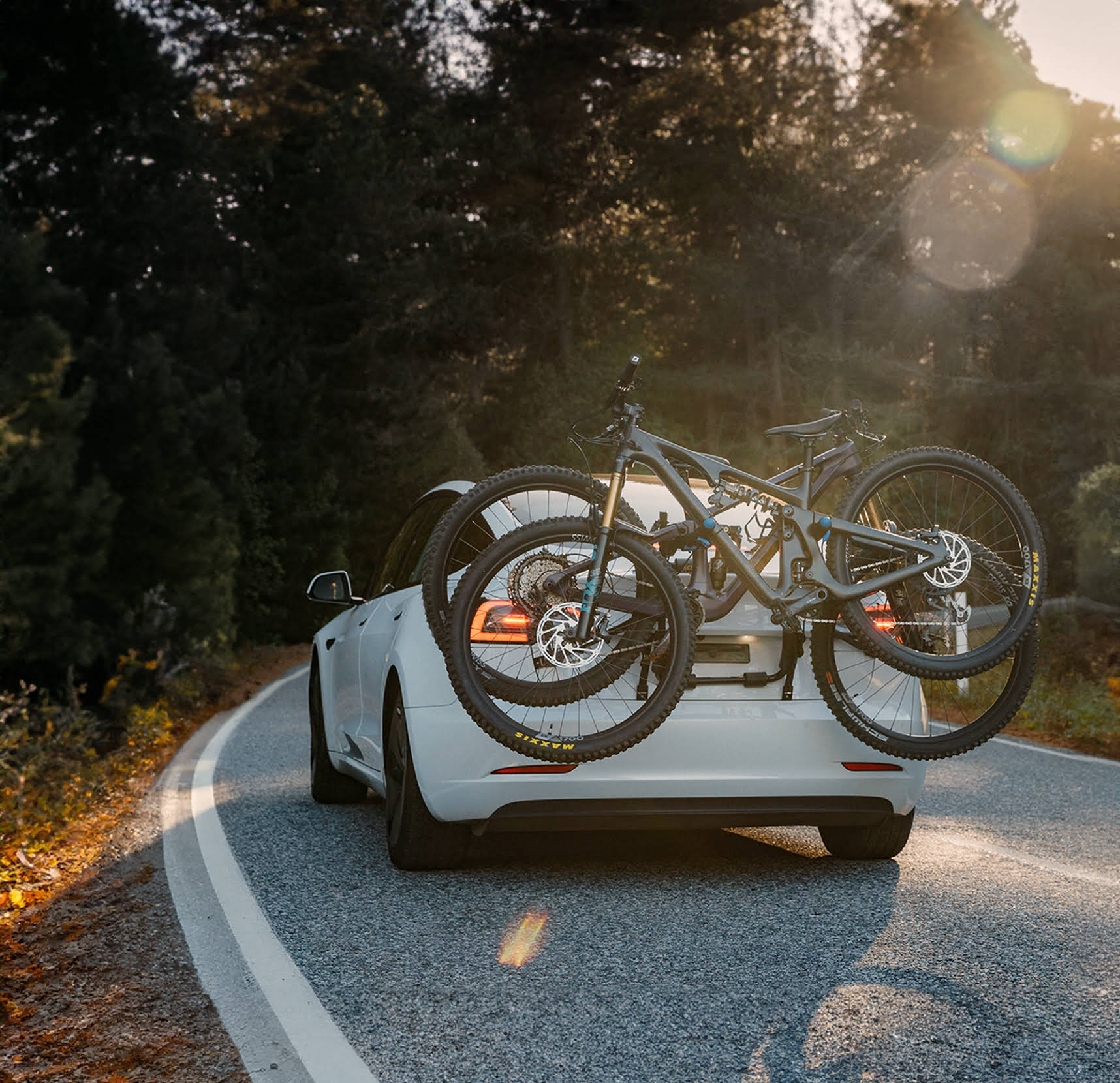 Two mountain bikes are strapped to a bootmounted bike rack on the back of an electric vehicle.