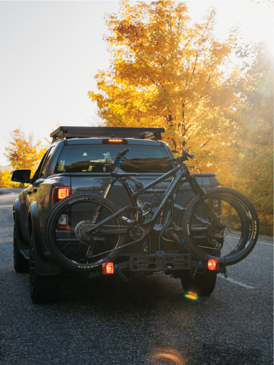 A view of an E-Rack 2 bike rack as it drives into the sunset in a New Zealand mountain with two electric bikes being carried and the tail lights clearly visible