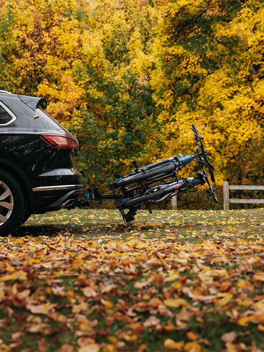 A side view of a vehicle with an E-Rack 2 tilted away from the vehicle for access to the tailgate. The bike rack is carrying two ebikes.