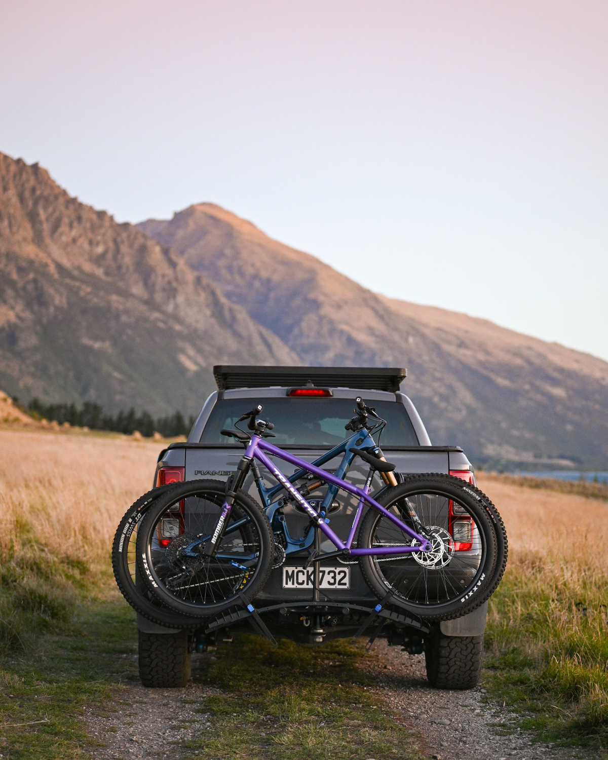 A rear view of the Enduro 2 bike rack without lightboard and two mountain bikes strapped to the bike rack. The bike rack is mounted to a ute and mountains are visible in the background