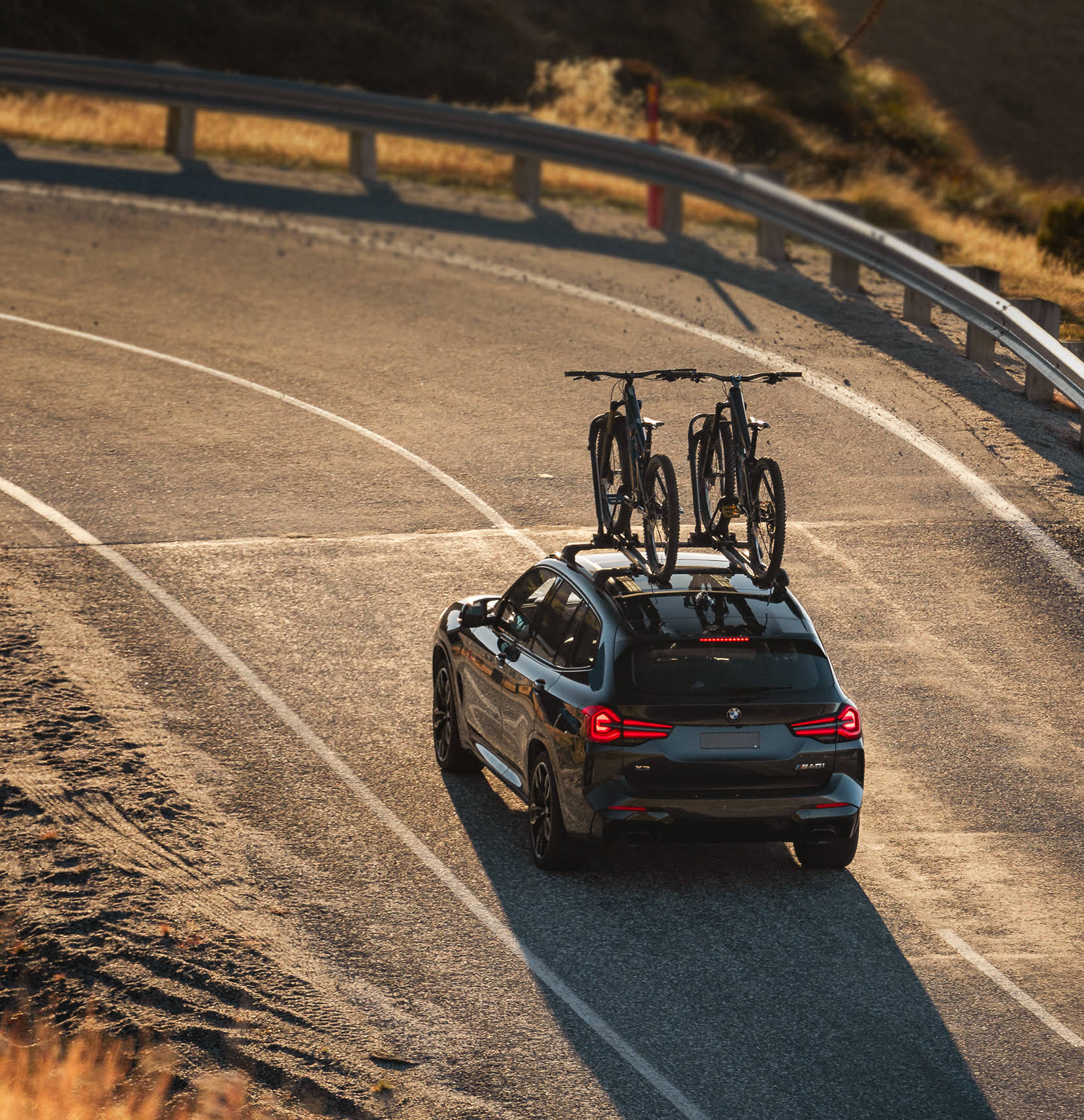 a SUV drives up a mountain road with two mountain bikes atop the roof - strapped into place using the Ezigrip Uplift 1