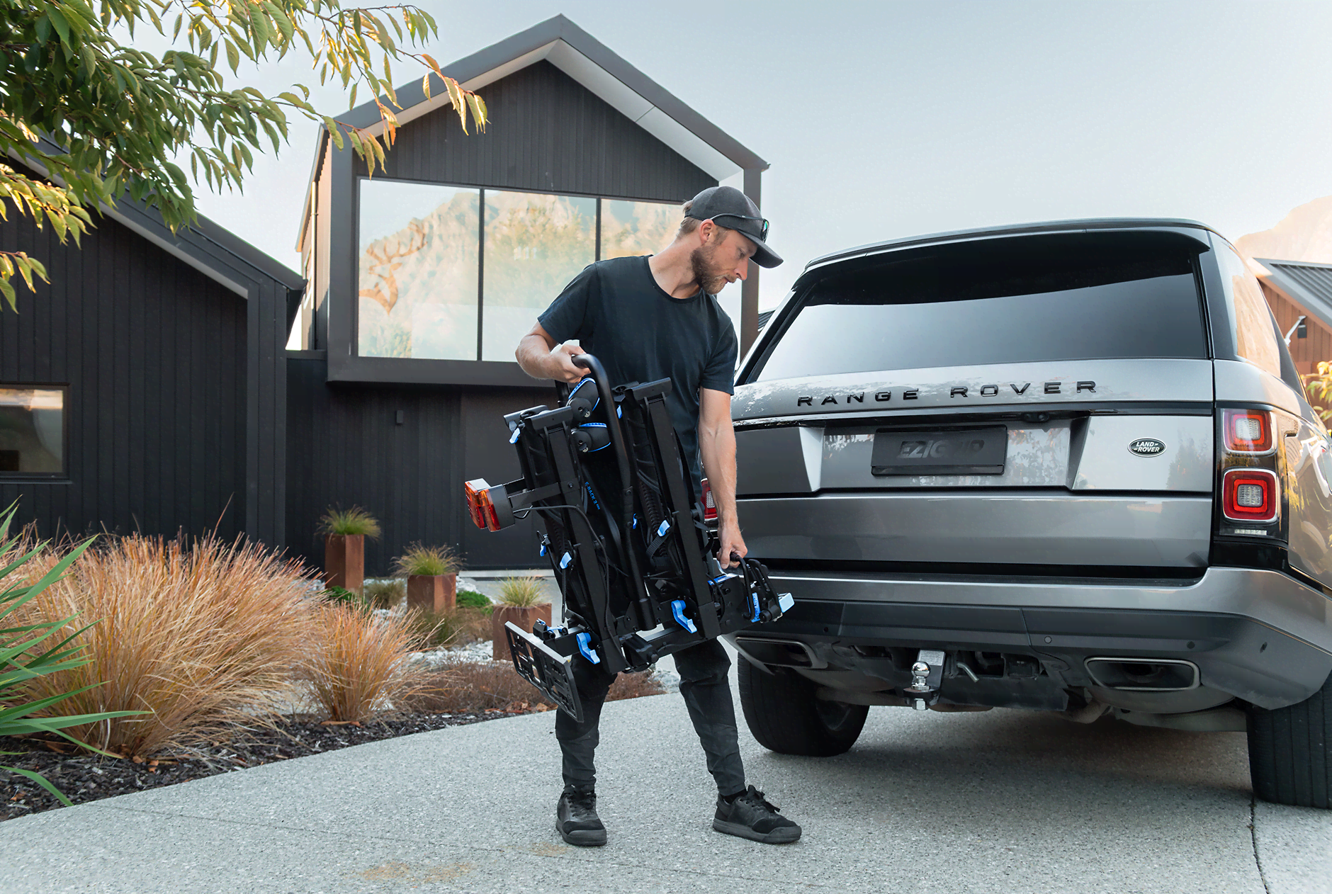 A man loads an E-Rack 2 Pro bike rack onto a Range Rover in front of his house