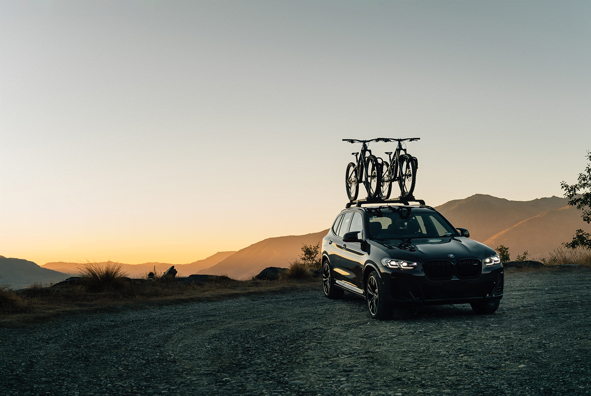 two bikes are sitting in roof mounted bike racks atop a SVU during sunrise