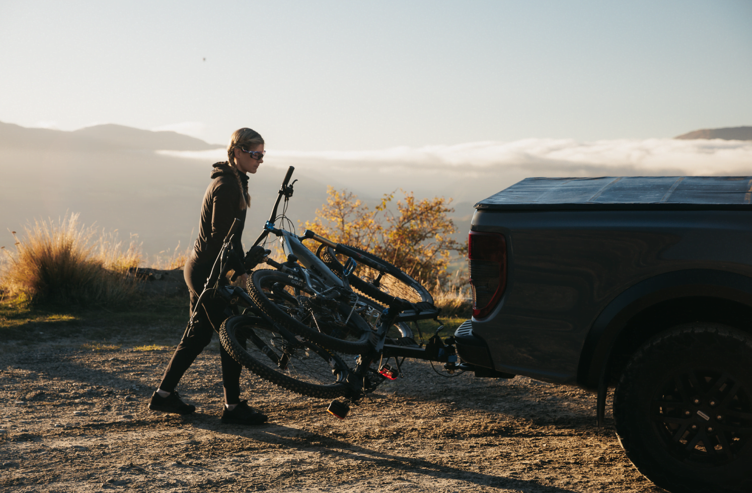 A woman is tilting a fully loaded e-bike rack, the Ezigrip E-Rack 2, which is mounted to the towball of a vehicle