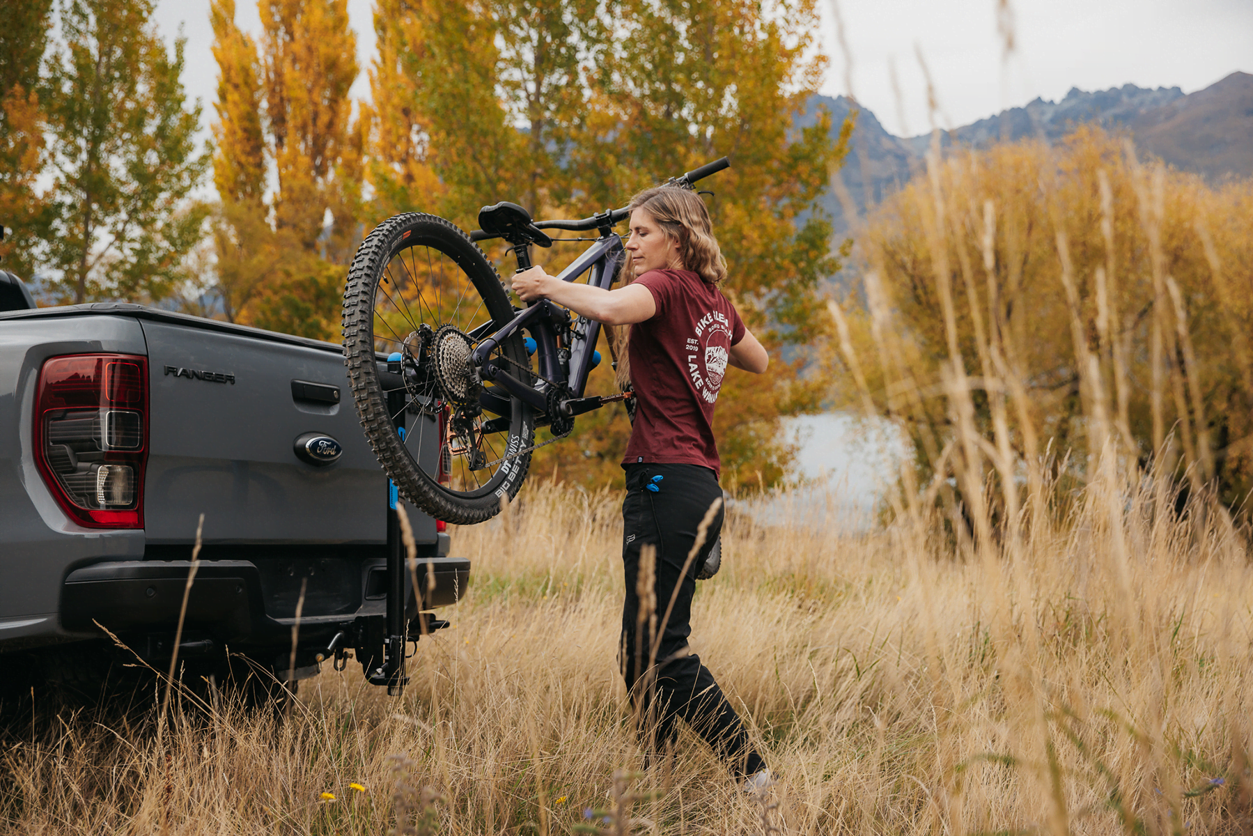 A woman is loading a mountain bike onto an Advantage 2 Prong Bike Rack that is mounted to the tow ball of a vehicle