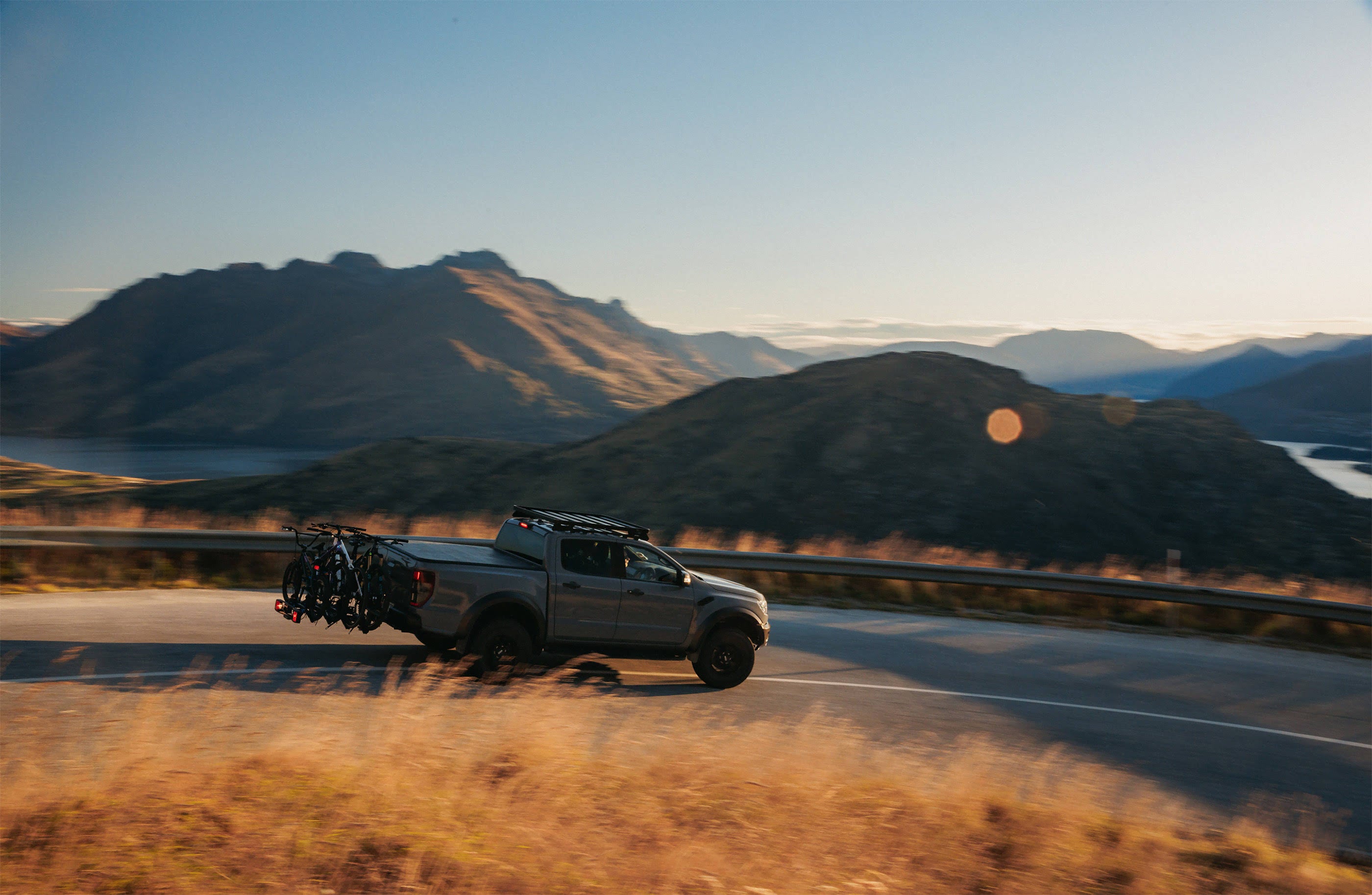 A ute is driving down a mountain road with 4 bikes being carried on the back using the Ezigrip Enduro 4 bike rack.