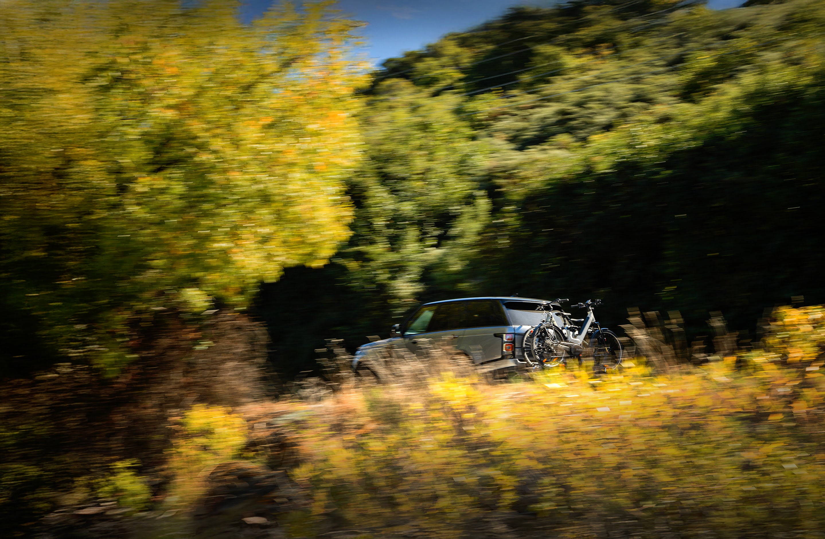 A SUV is streaking through the trees with two electric bikes (ebikes) clearly visible on the back, sitting atop a bike rack.
