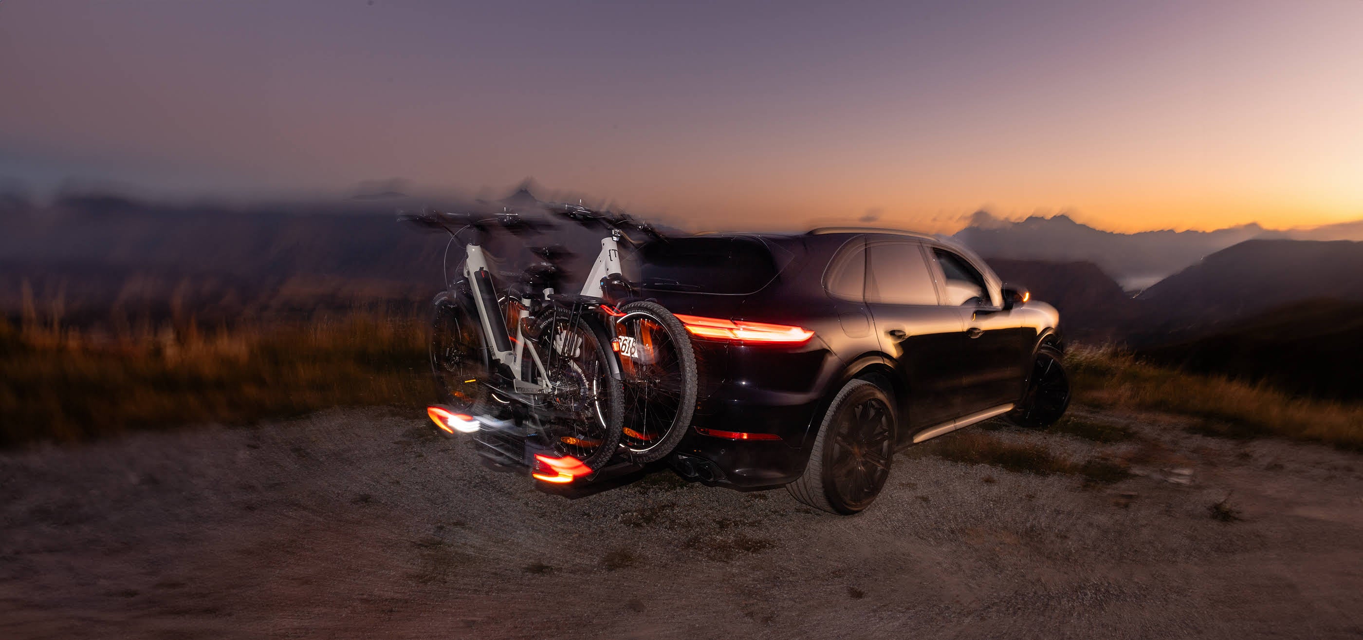 An Ezigrip E-volve 2 is mounted to the back of a Porsche SUV with the LED tail lights on the rack glowing in the sunset.