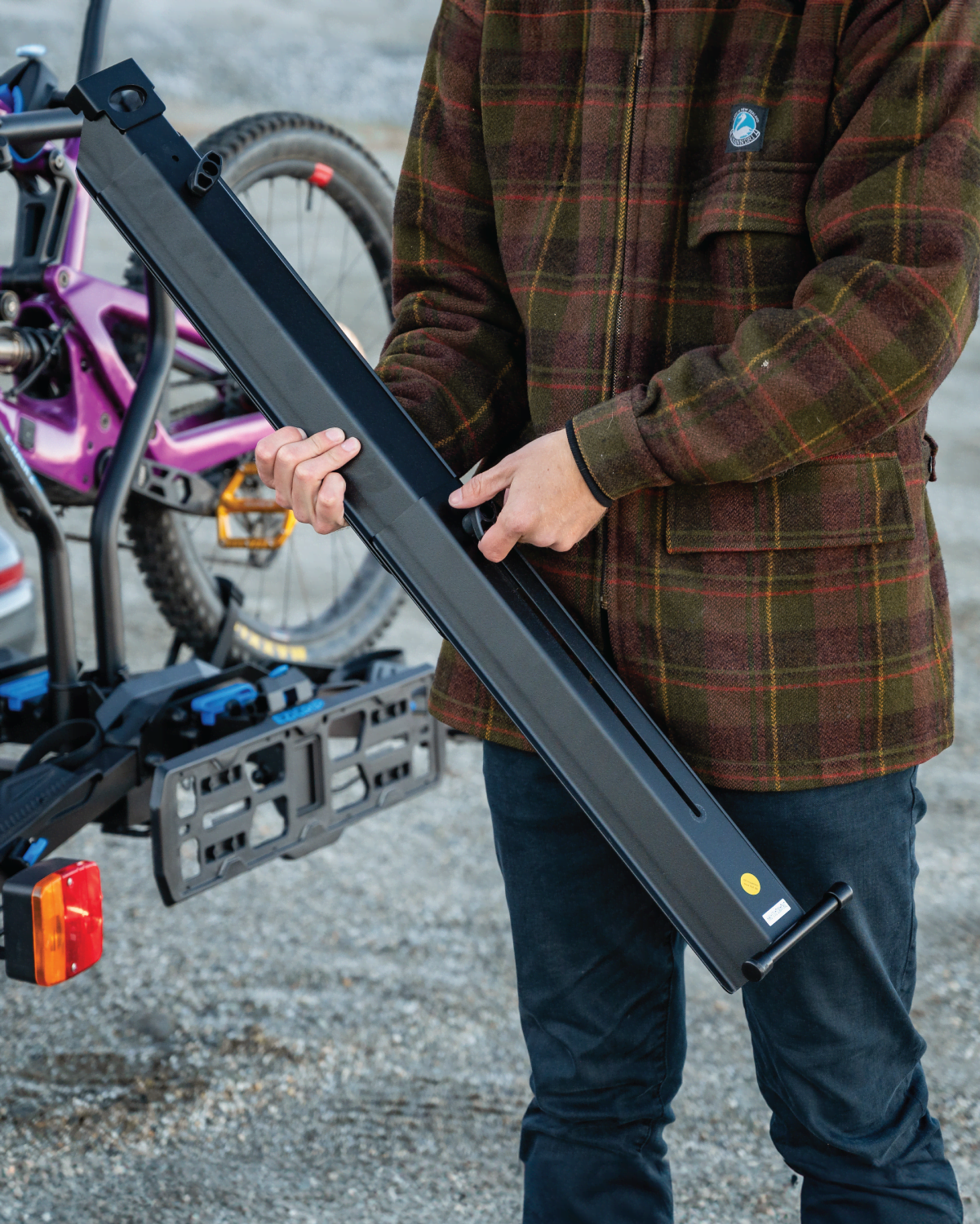 A man is extending the Ezigrip E-Rack 2 Pro Ramp using the wing nut and telescoping connection. Behind him is the E-Rack 2 Pro with an ebike loaded.